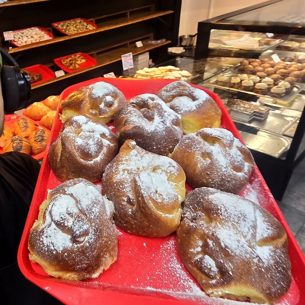 Choux cu cremă, pudrate cu zahăr, pe tava roșie